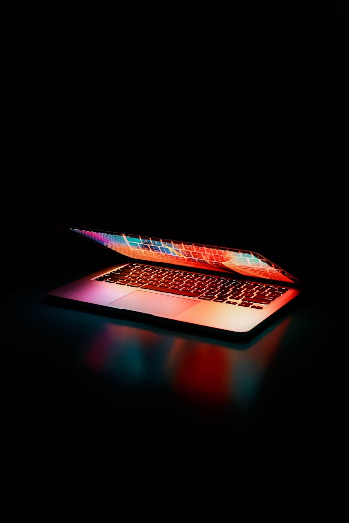 about-01 Laptop partially opened, emitting vibrant multicolored lights in dark setting.